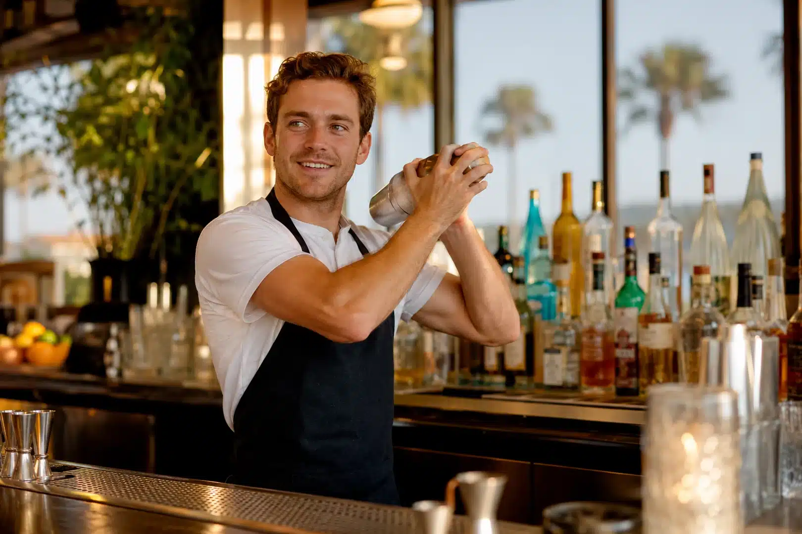 How to become a bartender in California — bartender shaking a cocktail behind a sunlit California bar.