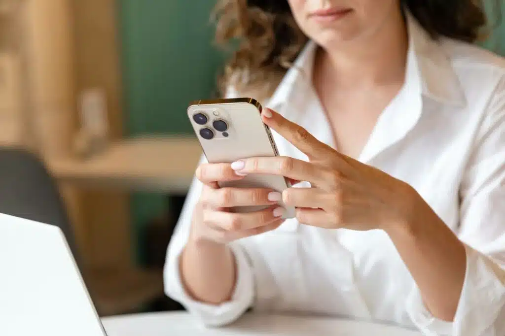 A person in a white shirt holds and looks at a light-colored smartphone.
