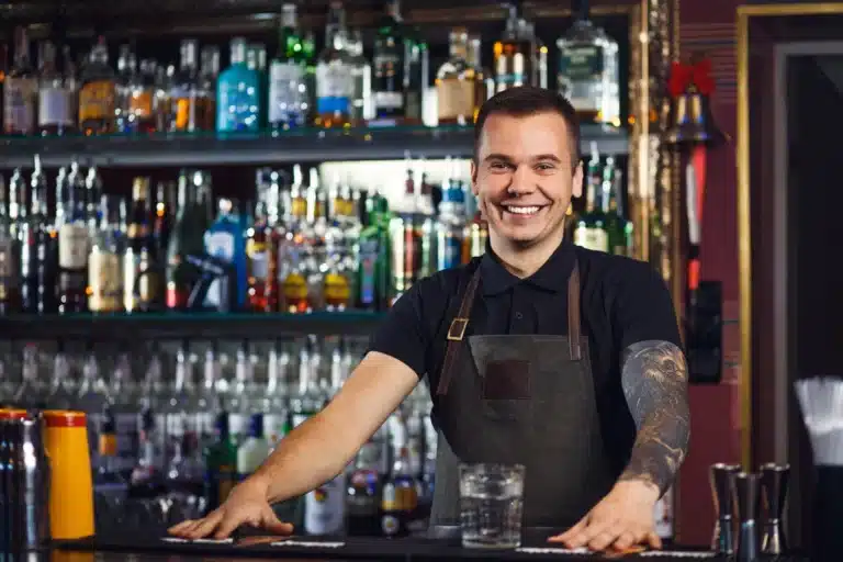 Smiling bartender behind a bar counter with liquor bottles, representing Missouri Bartending License training.