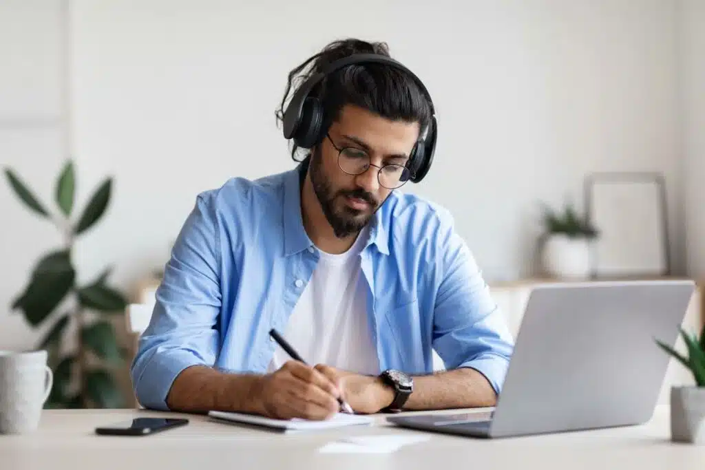 a man in headphones taking notes from an online course