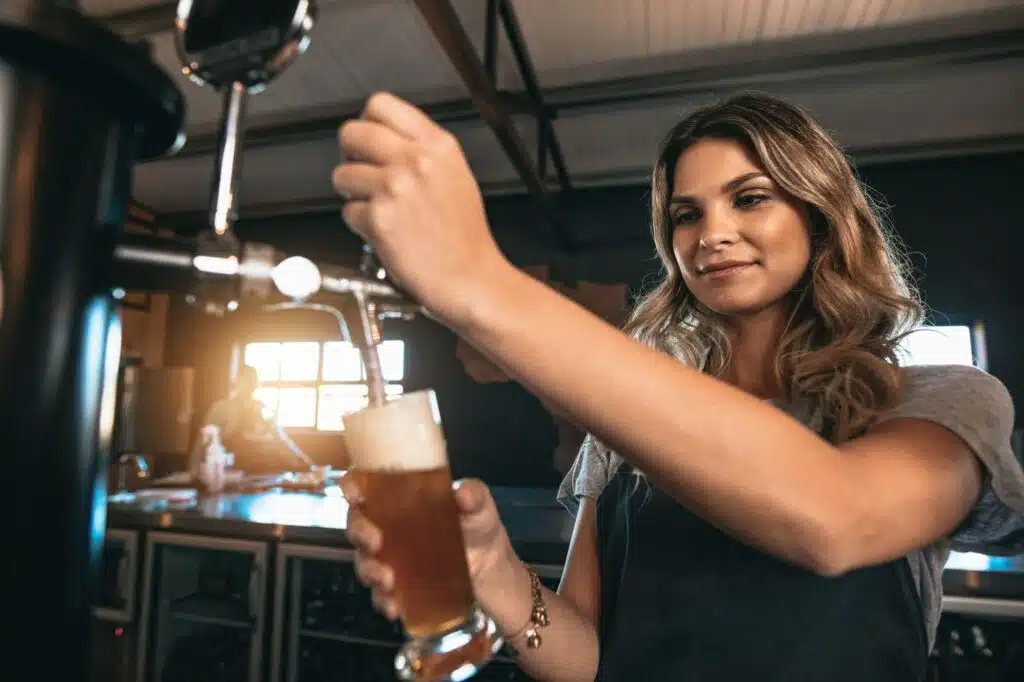 a smiling young female bartender pouring beer